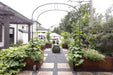 Backyard edible garden with climbing plants on metal arches, Corten steel raised beds, gravel path, and patio.