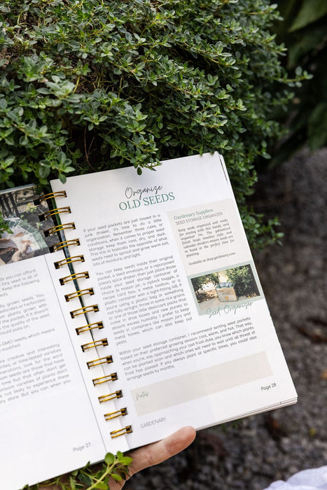 Gardening guide open to "Organize Old Seeds," showing seed storage tips, a seed organizer, and green herbs.