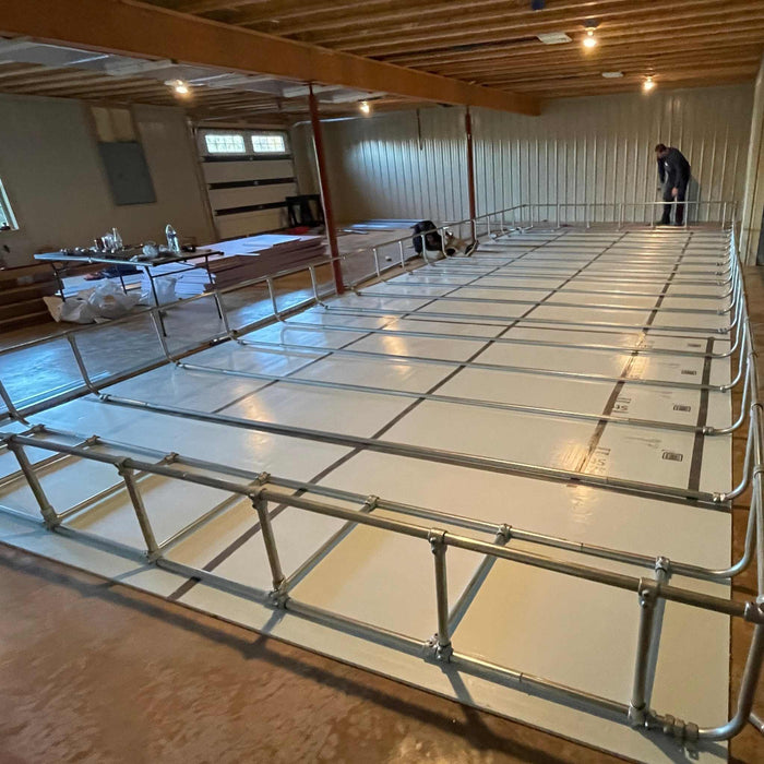 Basement renovation: white floor insulation panels, metal electrical conduit grid system, and worker.