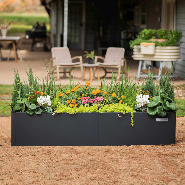 Modern black Vego Garden raised planter filled with vibrant flowers & foliage on gravel. Perfect for backyard gardening.