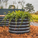 Corrugated metal garden planter with vibrant green plants cascading over wood chip mulch. Outdoor landscaping.