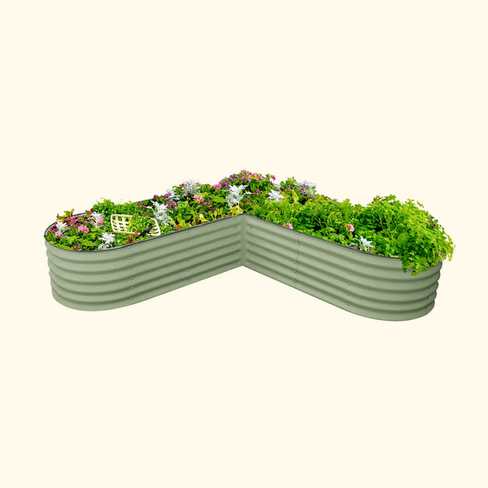 Sage green L-shaped corrugated steel raised garden bed with vibrant flowers, herbs, and a gardening basket.