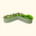 Sage green L-shaped corrugated steel raised garden bed with vibrant flowers, herbs, and a gardening basket.