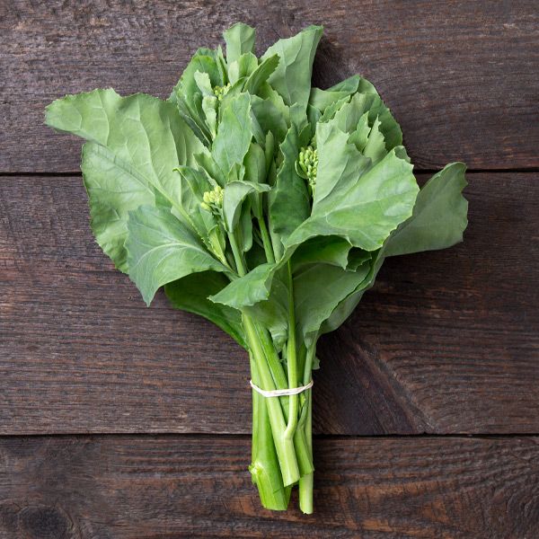 Fresh Chinese broccoli (Gai Lan) bunch with green leaves and small florets, tied with a band on dark wood.