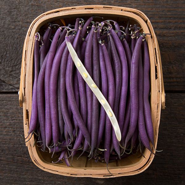 Basket of fresh purple string beans, one pod split open revealing seeds on wood.