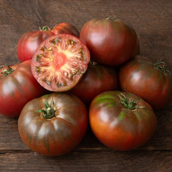 Fresh heirloom tomatoes, dark red-brown with green shoulders, one sliced open on wood. Garden produce.