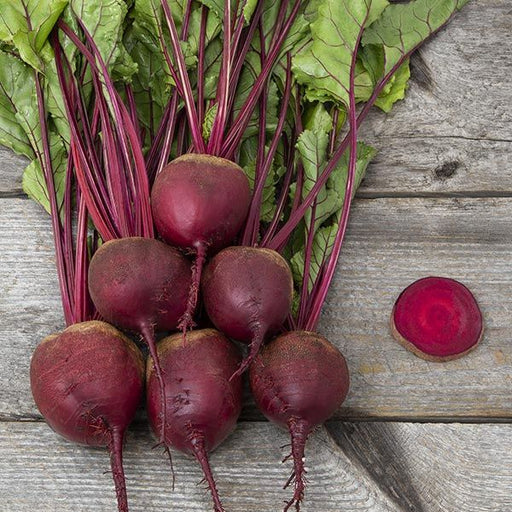 Vibrant red beets with green leaves and stems on rustic wood. One beet sliced, revealing its rich color.