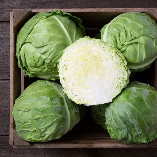 Fresh green cabbages, one cut open to show its white interior, in a rustic wooden crate. Healthy vegetables.