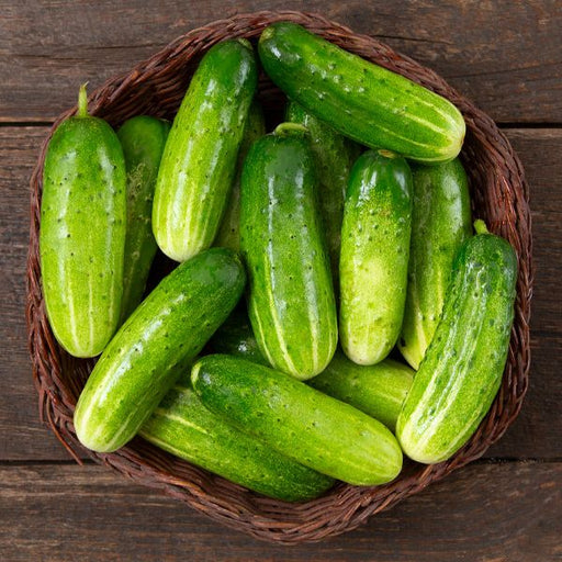 Fresh green cucumbers in a woven basket on a rustic wooden table.