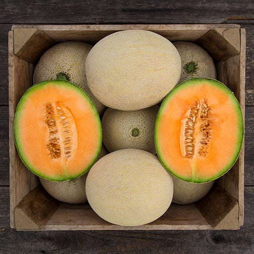 Fresh, ripe cantaloupe melons in a wooden crate. Two halves show vibrant orange flesh, seeds. Healthy sweet fruit.
