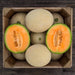 Fresh, ripe cantaloupe melons in a wooden crate. Two halves show vibrant orange flesh, seeds. Healthy sweet fruit.