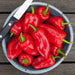 Fresh red mini sweet peppers in a blue bowl with a paring knife on a rustic wooden table.