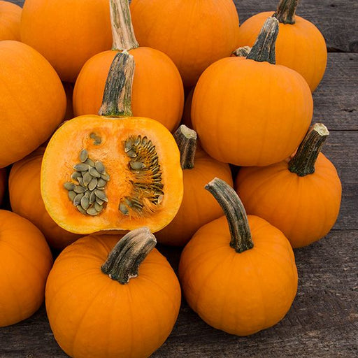 Small orange pumpkins, one cut showing seeds, on a rustic wooden surface. Great for autumn decor or baking.