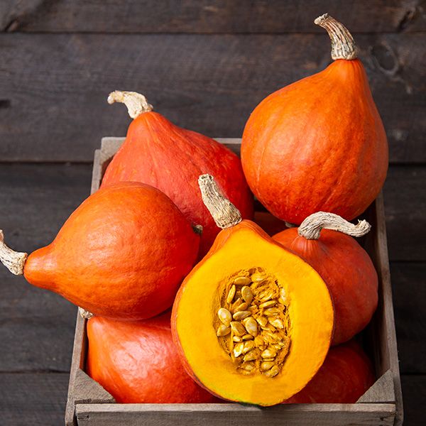 Red Kuri squash in a wooden crate, one cut to show seeds and orange flesh. Fresh fall harvest.