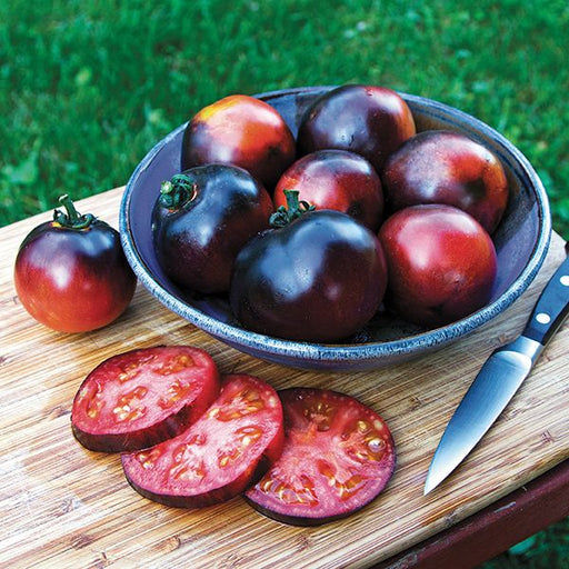 Harvested black and red heirloom tomatoes, whole in a bowl and sliced on a cutting board with a knife. Fresh garden produce.