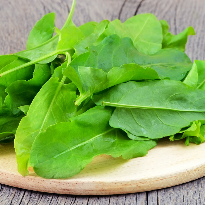 Freshly picked green sorrel leaves on a round wooden chopping board, rustic wood table.