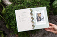 Open garden journal with planting, tending, harvesting sections. A hand holds it over lush green plants like thyme.