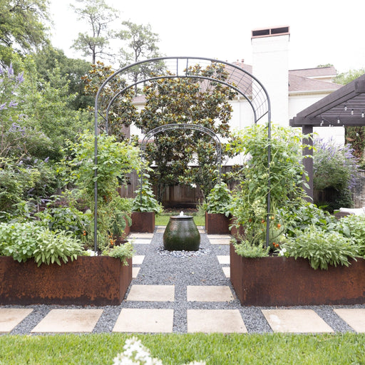 Modern backyard garden with corten steel raised vegetable beds, tomato plants, herbs, central fountain, gravel path, and pergola.