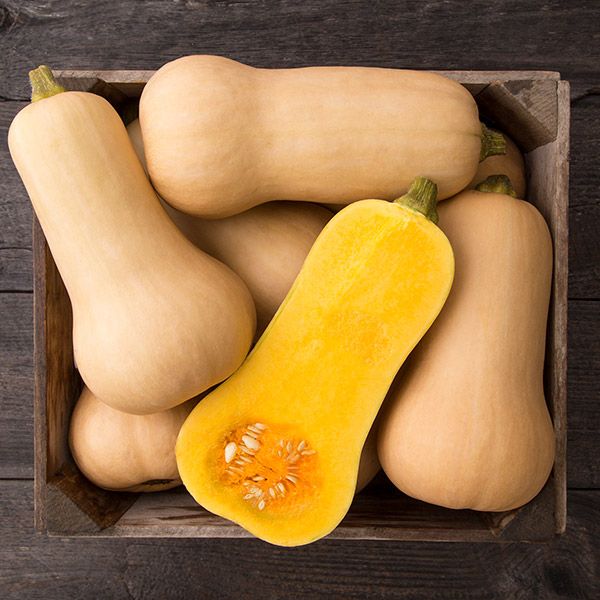 Butternut squash in wooden crate, one sliced open showing orange flesh & seeds. Fresh, healthy winter vegetable.