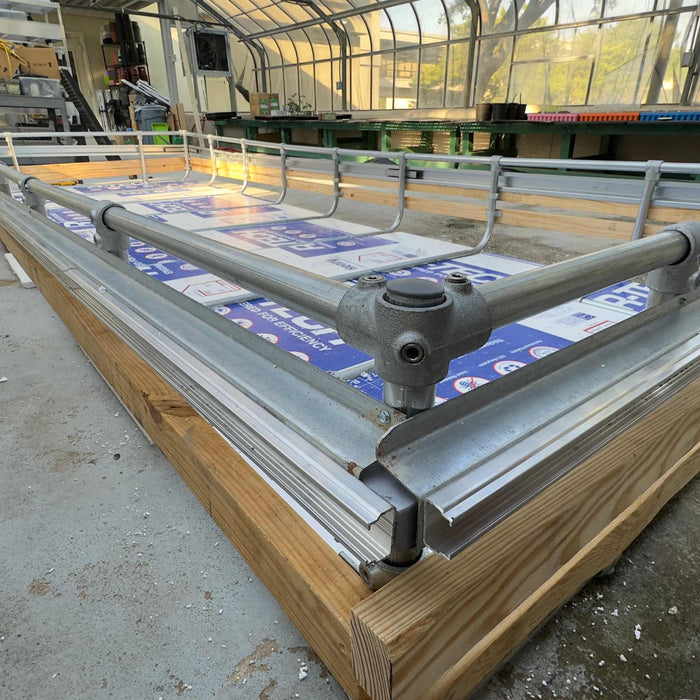 Greenhouse rolling bench with wood frame, metal rails, and blue protective sheeting, ready for plant cultivation.