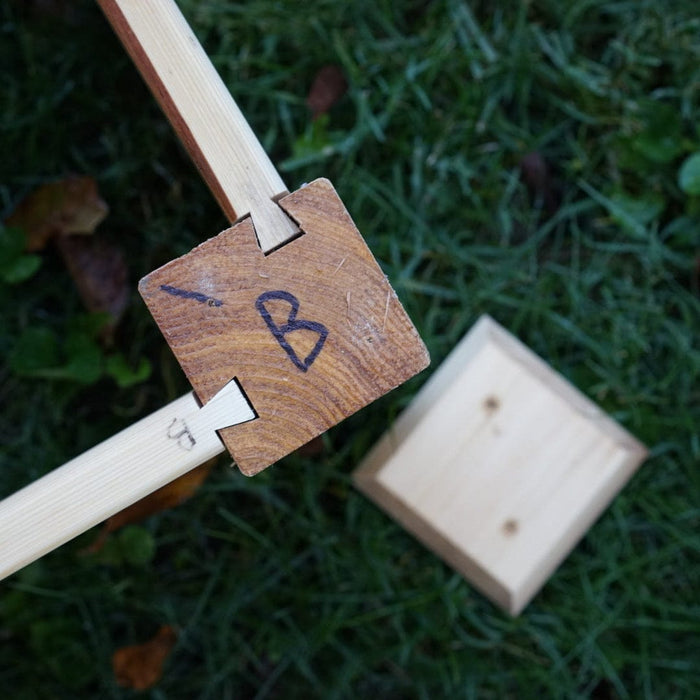 Woodworking dovetail joint on a marked wooden block "B" and stick, lying on grass. DIY carpentry assembly.