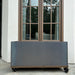 Corten steel mobile planter box on casters, placed by a brown window, white stucco wall, and stone patio.