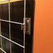 Silver metal mounting bracket securing a wire grid panel to a black board, attached to an orange wall.