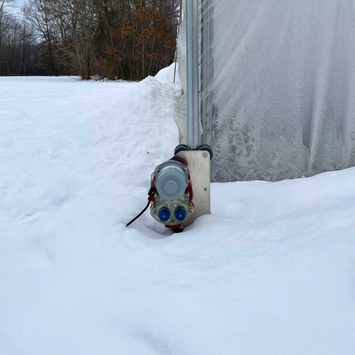 Automated greenhouse roll-up side wall motor on a high tunnel covered in snow. Efficient winter ventilation.