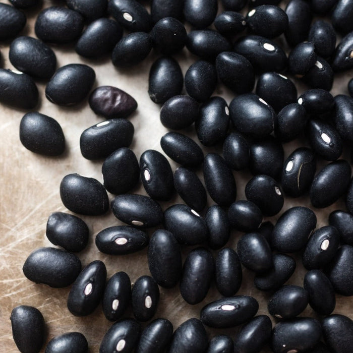 Close-up of dried black beans with visible white hilums, scattered on a light brown surface. Healthy plant-based ingredient.