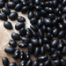 Close-up of dried black beans with visible white hilums, scattered on a light brown surface. Healthy plant-based ingredient.
