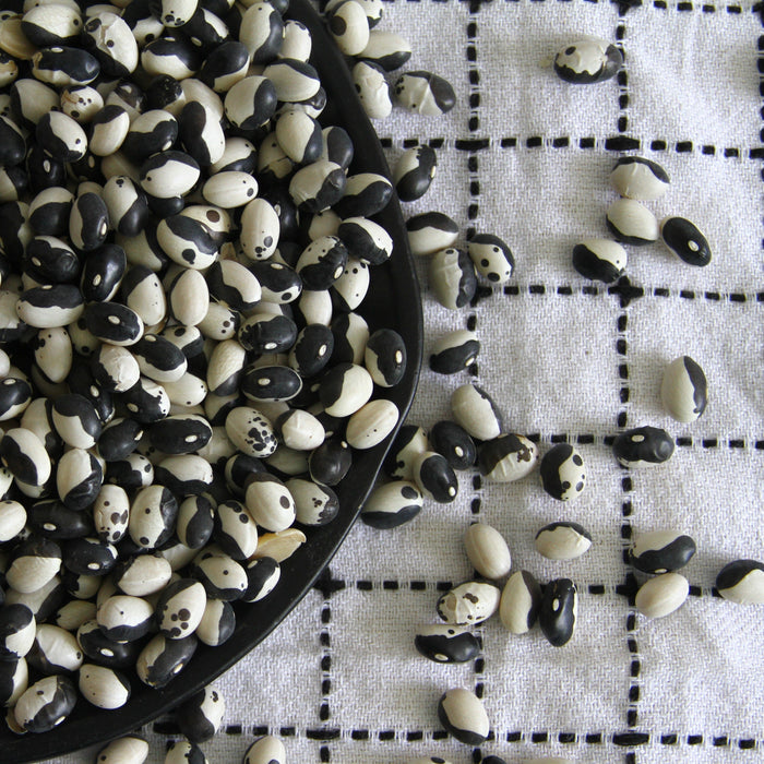 Black and white Yin Yang beans in a black bowl, spilled onto a white checkered tablecloth. Dried legumes for cooking.