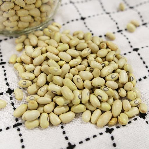 Pale green dried beans with black eyes scattered on a white checkered tablecloth. Healthy protein source, legumes.