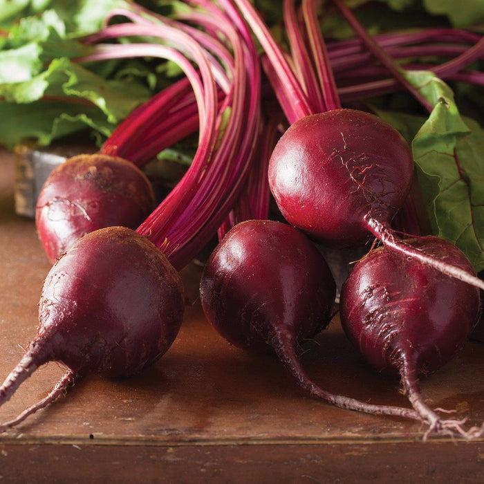 Fresh dark red beets with vibrant green tops and roots on a rustic wooden surface.