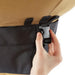 Hand securing a black quick-release buckle on a tan and black fabric strap. Durable closure for bags, covers, gear.