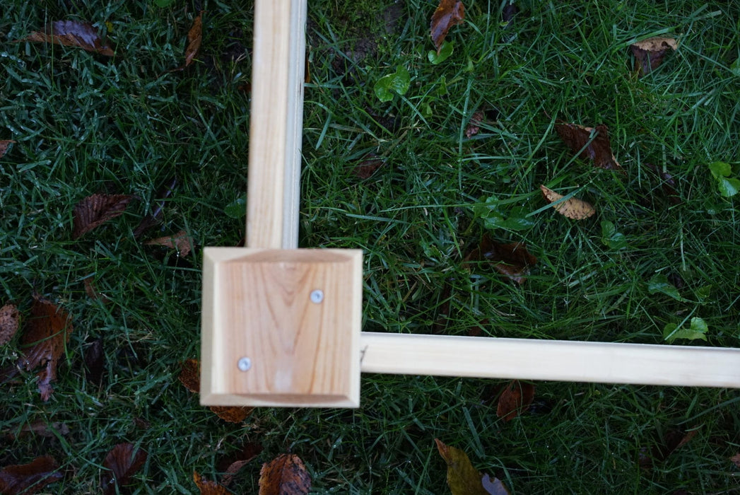Wooden frame corner joint with screws on green grass and autumn leaves. Outdoor DIY construction.