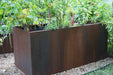 Corten steel raised garden bed with diverse green plants, herbs, and colorful flowers, set on gravel.