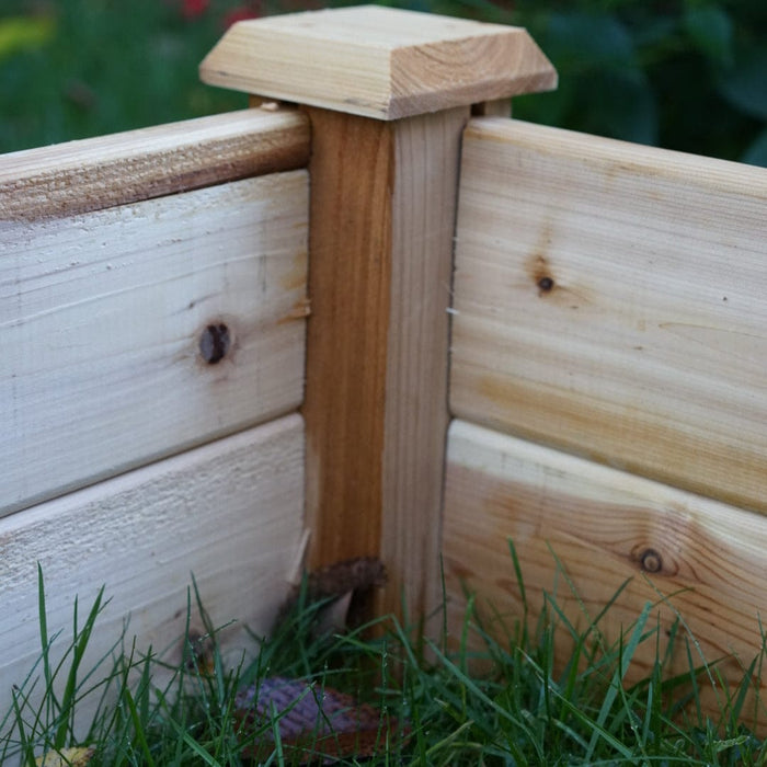 Cedar raised garden bed corner with decorative post cap and green grass.