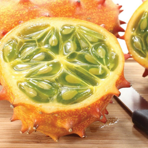 Cut horned melon (kiwano) revealing juicy green pulp. Spiky orange African horned cucumber on wooden board with knife.
