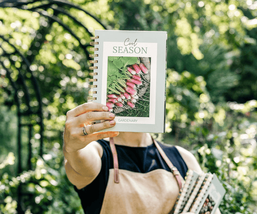 Gardenary "Cool Season" radishes planting journal held by a gardener in a lush outdoor garden.