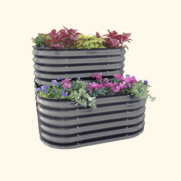 Dark grey two-tier corrugated metal raised garden bed with red coleus, pink cyclamen, and purple pansies.