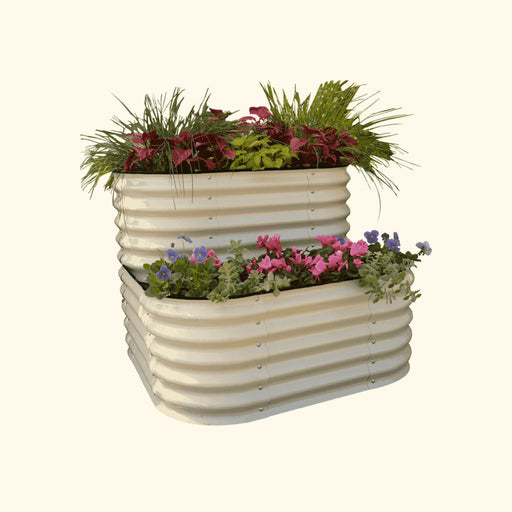 Tiered beige corrugated steel raised garden bed with vibrant red coleus, green grass, pink cyclamen, and purple pansies.