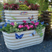 Vego Garden tiered corrugated metal raised garden bed with pink cyclamen, blue pansies, coleus, and animal stickers. Stone fountain.