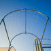Metal hoop house frame with plant trellis netting under a clear blue sky. Garden structure for climbing plants.