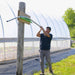 Farmer adjusts high tunnel greenhouse ventilation arm. Crops growing inside farm structure.