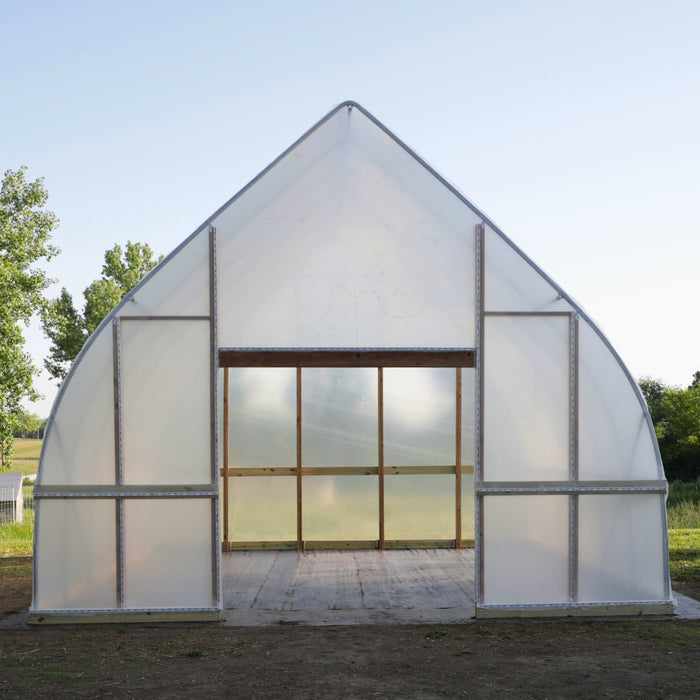 New white plastic high tunnel greenhouse. Arched hoop house structure with a wooden framed entrance for gardening.
