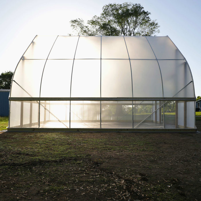 New translucent hoop house greenhouse with curved roof, bright sunlight inside, on a dirt field. Ideal for farming.