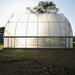New translucent hoop house greenhouse with curved roof, bright sunlight inside, on a dirt field. Ideal for farming.
