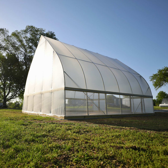Spacious white poly-covered hoop house greenhouse on a green farm field, clear sky. Modern agricultural growing structure.