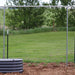 Dark gray corrugated metal raised garden bed with a galvanized steel frame, young plants, wire fence, and green field.