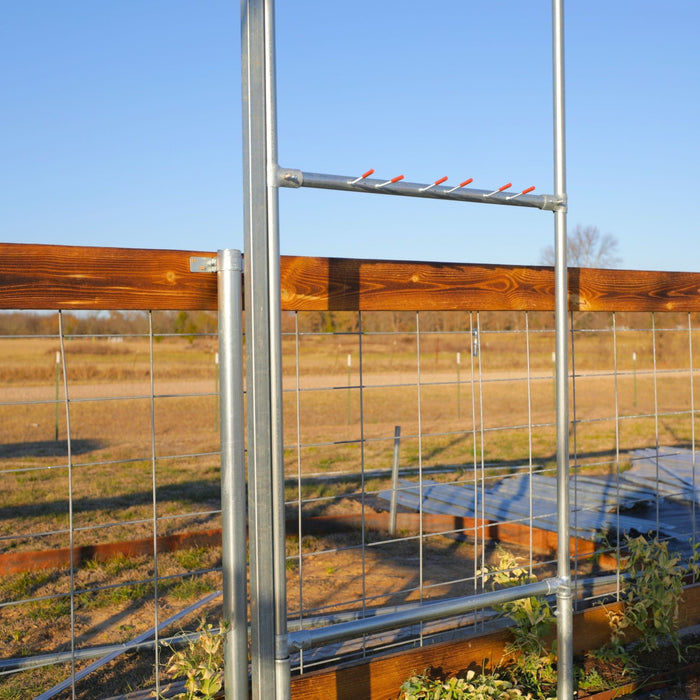 Galvanized steel garden trellis with orange hooks, wooden top rail, and wire mesh fence over a raised bed with plants.